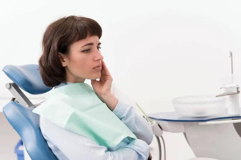 This shows a patient with clear signs of pain on the left side of her mouth in a dentist chair